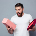 Portrait of a young man opening gift box over gray background
